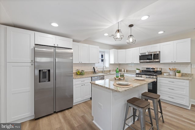 kitchen with light wood-type flooring, sink, white cabinets, a kitchen island, and appliances with stainless steel finishes