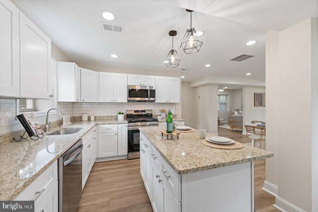 kitchen with hanging light fixtures, white cabinetry, stainless steel appliances, light hardwood / wood-style flooring, and sink