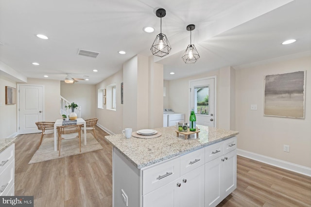 kitchen featuring decorative light fixtures, light wood-type flooring, washer and dryer, and white cabinetry