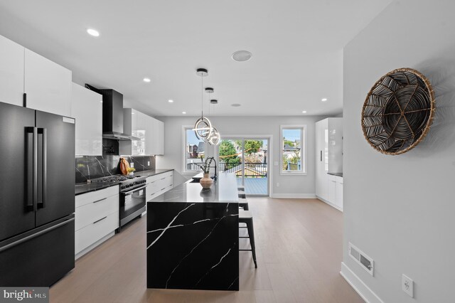 kitchen featuring high end appliances, light wood-type flooring, white cabinetry, pendant lighting, and a center island with sink