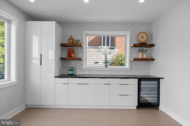 bar with light wood-type flooring, white cabinets, and wine cooler