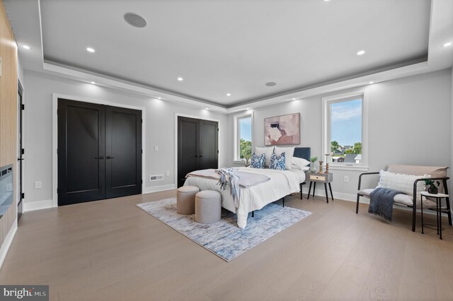 bedroom with light wood-type flooring, multiple windows, and a tray ceiling