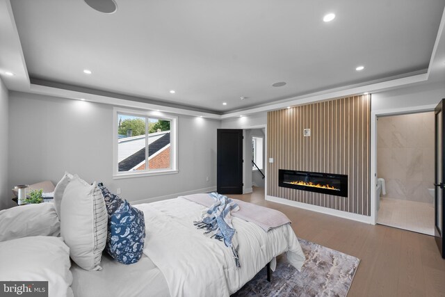 bedroom with a tray ceiling, hardwood / wood-style floors, and a large fireplace