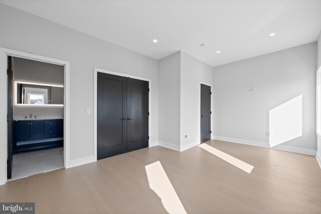 unfurnished bedroom featuring connected bathroom, sink, and light hardwood / wood-style floors