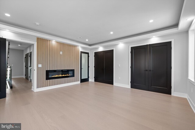 unfurnished living room with light wood-type flooring, a tray ceiling, and a large fireplace