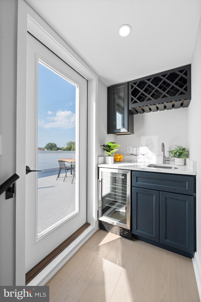 bar featuring light wood-type flooring, wine cooler, and sink