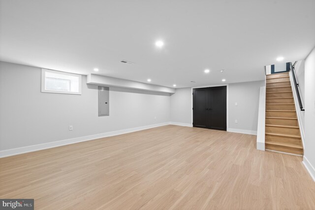 basement featuring electric panel and light hardwood / wood-style floors