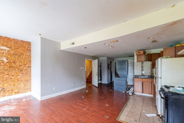 kitchen with white gas range, dark wood-type flooring, and brick wall