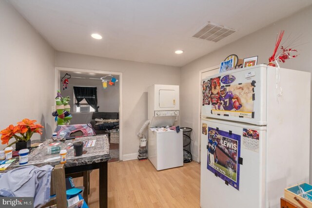 kitchen with light wood-type flooring, stacked washing maching and dryer, and white fridge