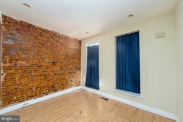 empty room featuring wood-type flooring and brick wall