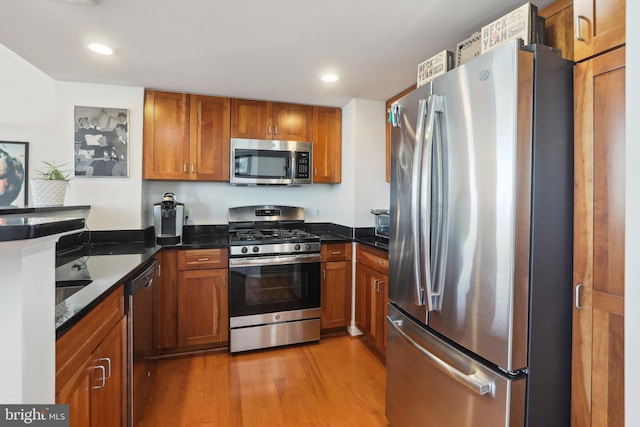 kitchen with stainless steel appliances, dark stone counters, and light hardwood / wood-style flooring