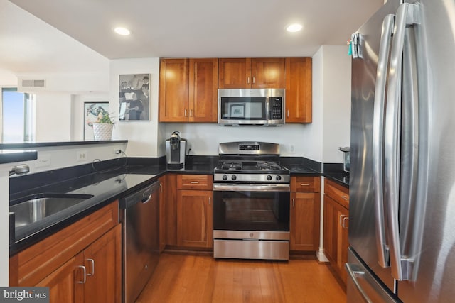 kitchen featuring appliances with stainless steel finishes, kitchen peninsula, sink, light wood-type flooring, and dark stone counters