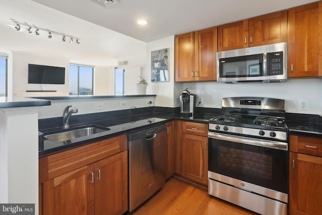 kitchen featuring stainless steel appliances, sink, kitchen peninsula, dark stone countertops, and light wood-type flooring