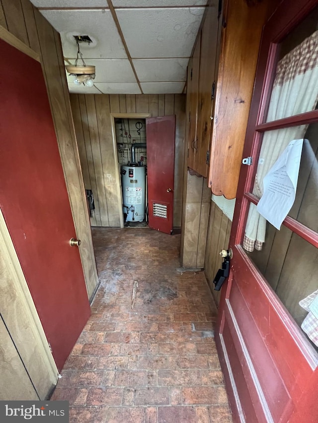 corridor with water heater, a paneled ceiling, and wooden walls