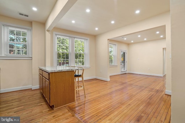 kitchen with a kitchen bar, light stone counters, and light hardwood / wood-style flooring