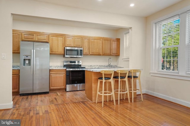 kitchen with light hardwood / wood-style flooring, light stone counters, stainless steel appliances, kitchen peninsula, and a breakfast bar