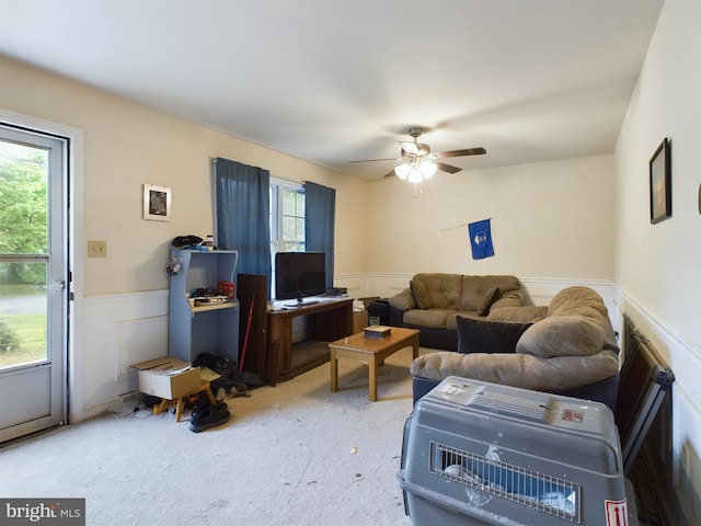 carpeted living room featuring a decorative wall, a ceiling fan, and a wainscoted wall