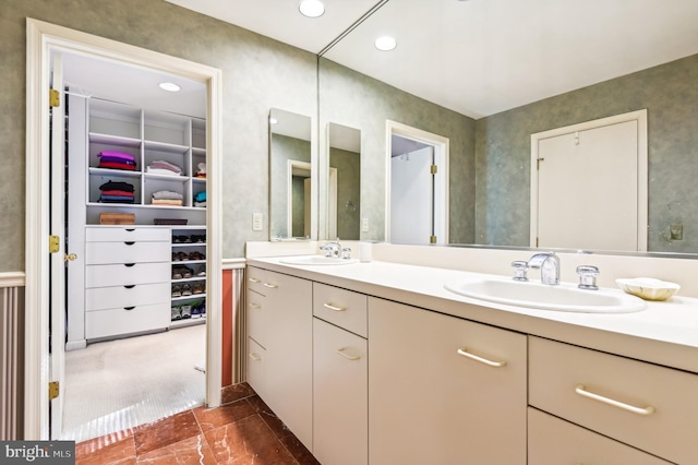 bathroom with a walk in closet, recessed lighting, double vanity, and a sink