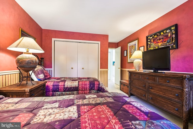 carpeted bedroom with a wainscoted wall and a closet