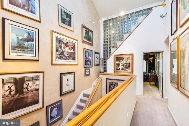 corridor with carpet floors, plenty of natural light, baseboards, stairway, and a towering ceiling