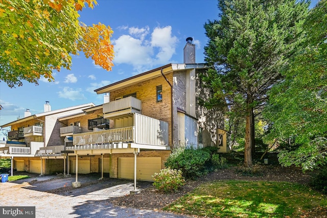 rear view of property featuring a balcony, a chimney, driveway, brick siding, and an attached garage