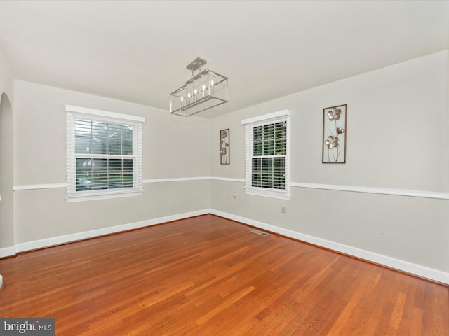 empty room with wood-type flooring and an inviting chandelier