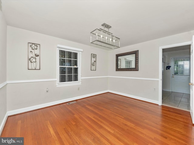 spare room with wood-type flooring and a chandelier