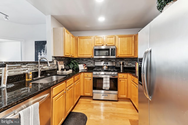 kitchen featuring decorative backsplash, light hardwood / wood-style floors, dark stone countertops, stainless steel appliances, and sink