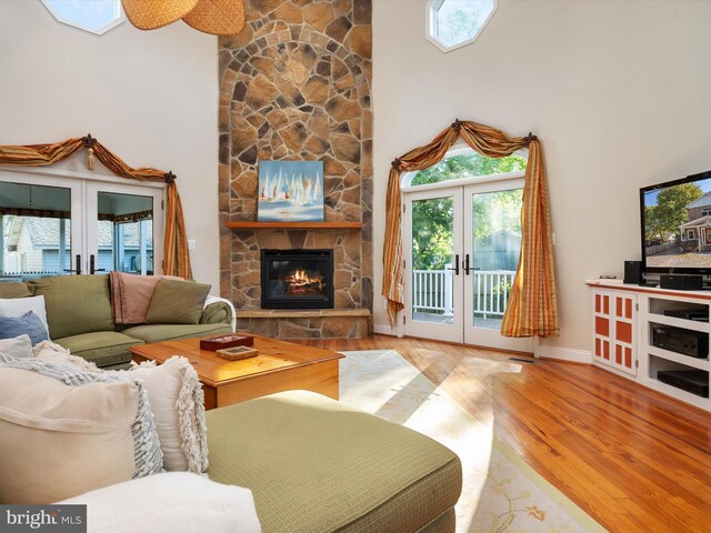 living room featuring a fireplace, a towering ceiling, french doors, and light hardwood / wood-style floors