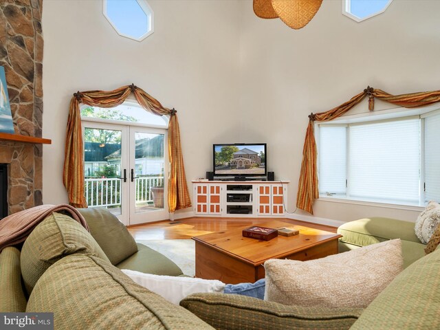 living room with light hardwood / wood-style flooring, french doors, ceiling fan, and a stone fireplace