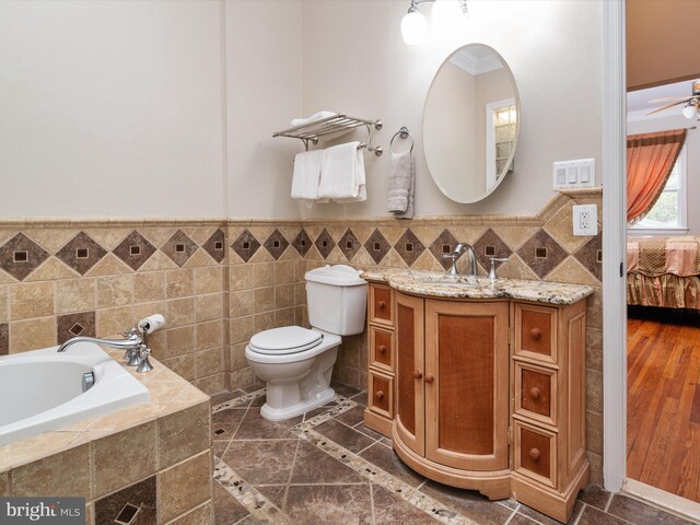 bathroom featuring vanity, tile walls, toilet, a relaxing tiled tub, and ceiling fan