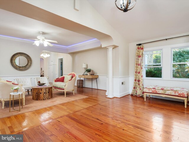 living area featuring hardwood / wood-style floors, ceiling fan with notable chandelier, decorative columns, and vaulted ceiling