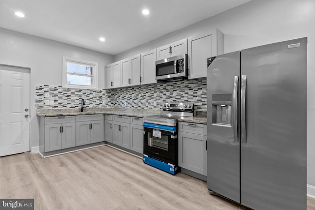 kitchen featuring tasteful backsplash, light stone countertops, appliances with stainless steel finishes, and light hardwood / wood-style floors