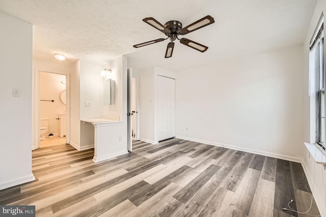 unfurnished bedroom featuring ensuite bath, ceiling fan, light hardwood / wood-style flooring, a textured ceiling, and a closet