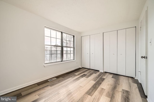 unfurnished bedroom with multiple closets and light hardwood / wood-style flooring