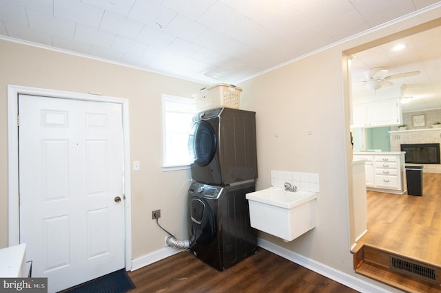 washroom featuring a fireplace, stacked washer and dryer, sink, ceiling fan, and dark wood-type flooring