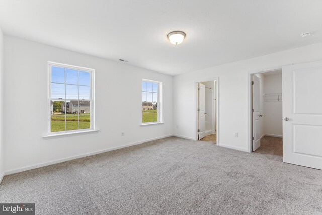 unfurnished bedroom with light carpet, a walk in closet, a closet, and multiple windows