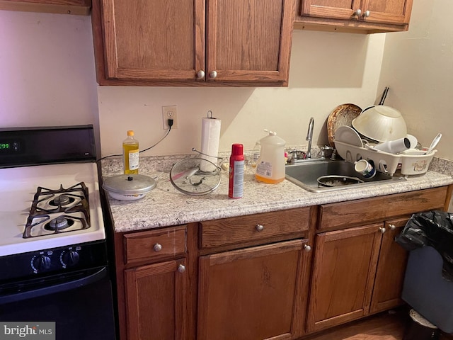 kitchen with dishwasher, light stone counters, white range with gas stovetop, and sink