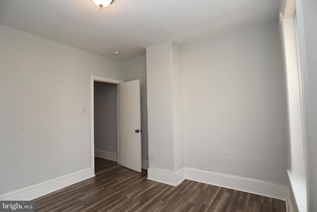 spare room featuring baseboards and dark wood-type flooring