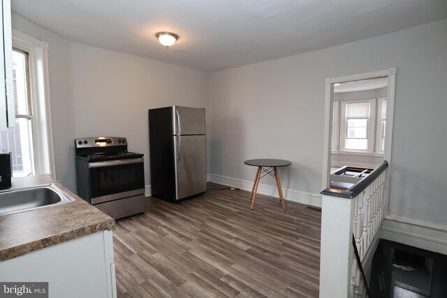 kitchen with hardwood / wood-style floors, appliances with stainless steel finishes, white cabinetry, and sink