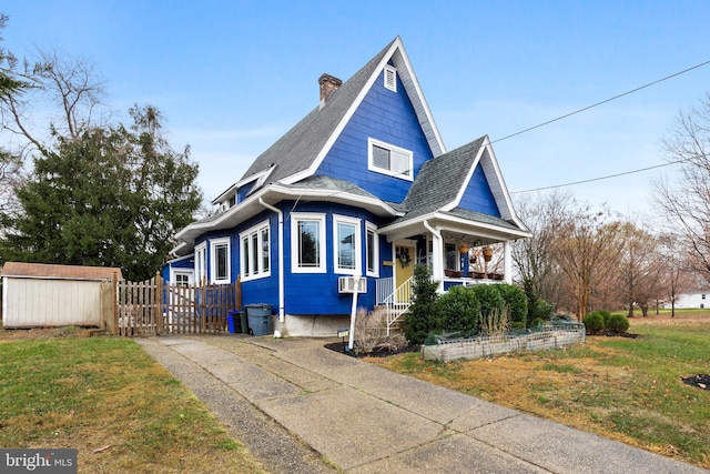 view of front of home with cooling unit, a front lawn, covered porch, and a storage shed