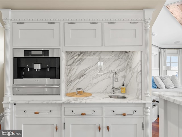 kitchen with white cabinetry, backsplash, wood-type flooring, sink, and light stone countertops