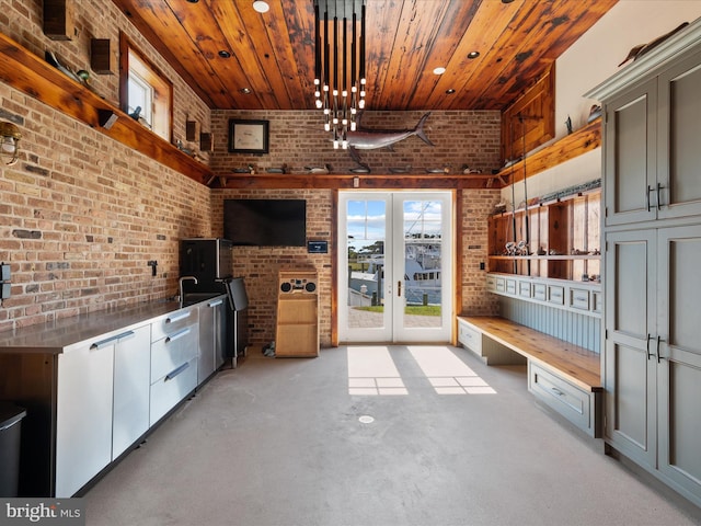 kitchen with gray cabinetry, french doors, decorative light fixtures, wood ceiling, and brick wall