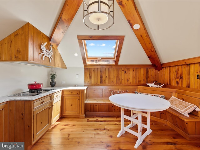 kitchen featuring wood walls, vaulted ceiling with skylight, light hardwood / wood-style floors, and stainless steel gas stovetop