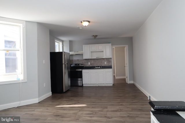 kitchen with dark hardwood / wood-style flooring, appliances with stainless steel finishes, white cabinetry, and extractor fan