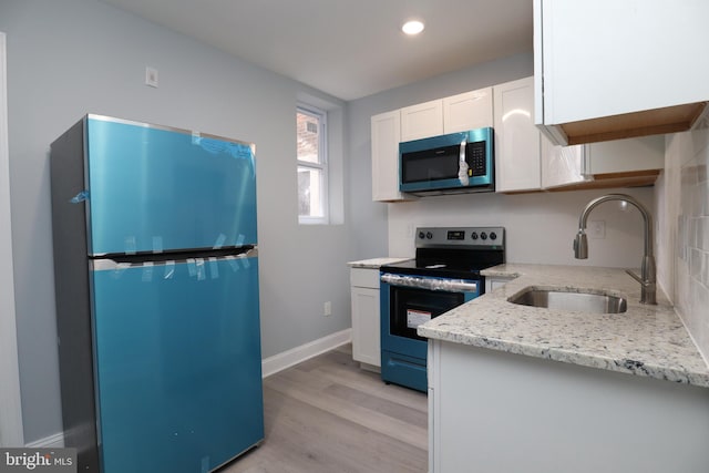 kitchen featuring light stone counters, sink, appliances with stainless steel finishes, white cabinets, and light hardwood / wood-style floors