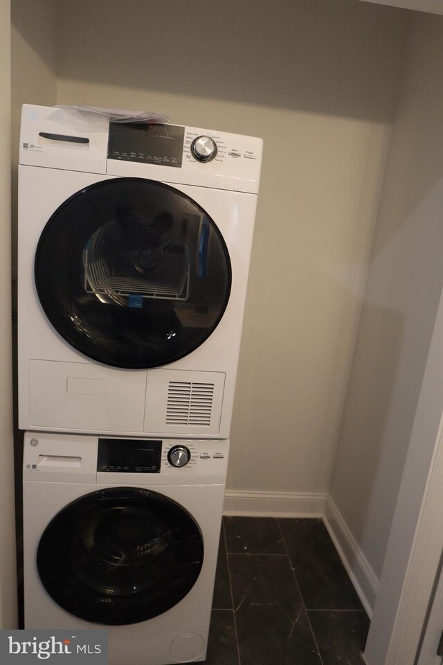 washroom with stacked washer and clothes dryer and dark tile patterned flooring