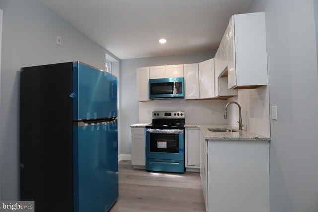 kitchen with light hardwood / wood-style flooring, sink, light stone countertops, appliances with stainless steel finishes, and white cabinets