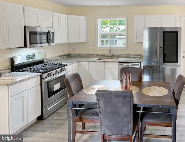 kitchen with light stone countertops, stainless steel appliances, sink, light hardwood / wood-style flooring, and white cabinets