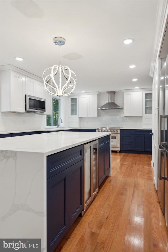 kitchen with wall chimney range hood, blue cabinets, stainless steel appliances, and white cabinetry